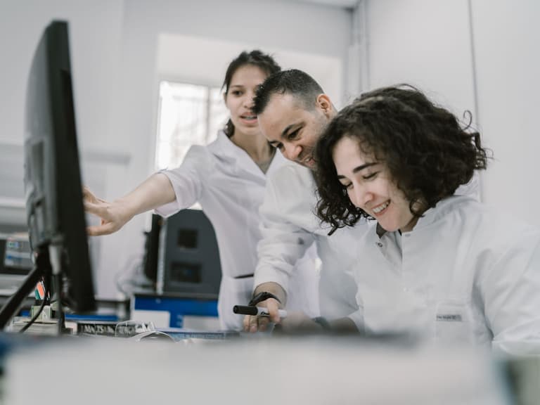 Trois professionnels de laboratoire en blouse blanche discutant devant un ordinateur