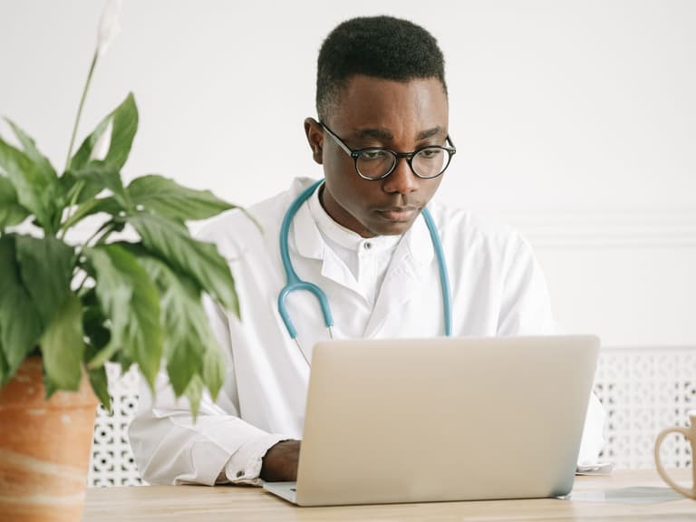 Médecin en blouse blanche consultant un dossier sur son ordinateur portable