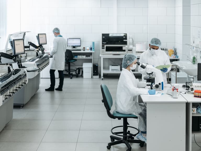 Vue d'ensemble d'un laboratoire clinique lumineux avec une rangée d'analyseurs automatisés et du personnel au travail