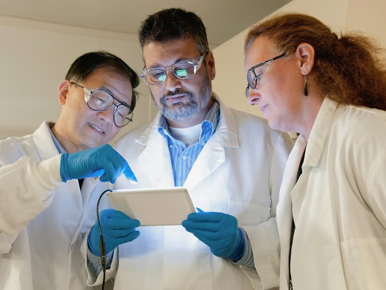 Trois scientifiques en blouse consultant ensemble une tablette dans un laboratoire