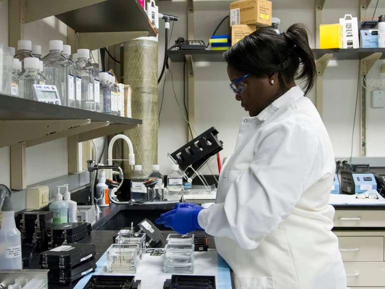 Technicienne de laboratoire en blouse et lunettes de protection travaillant à la paillasse
