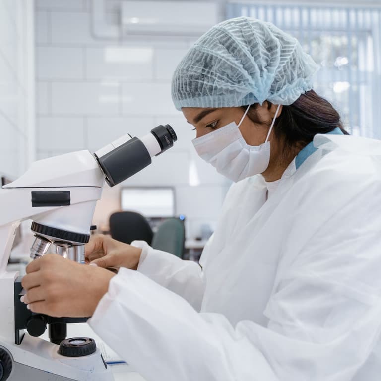 Technologue en tenue de protection réglant la mise au point d'un microscope